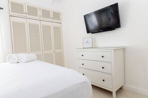 Une chambre bien rangée, avec un lit, une commode et un téléviseur fixé au mur.