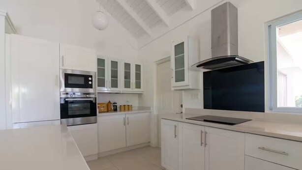 A modern kitchen with white cabinetry, stainless steel appliances, and a large window providing natural light. - Eshae Living - Uniquely Modern Beach House 3 (Plantation Village)