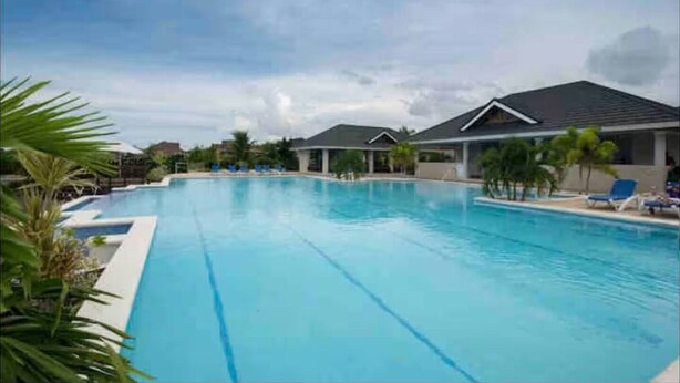 A large swimming pool with clear blue water, surrounded by lounge chairs and palm trees. - Eshae Living - Uniquely Modern Beach House 3 (Plantation Village)