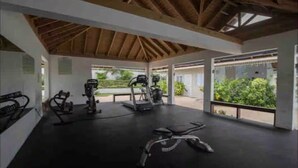 A covered gym area with exercise equipment, large windows, and a wooden ceiling. - Eshae Living - Uniquely Modern Beach House 3 (Plantation Village)