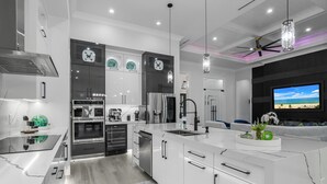 A modern kitchen with white cabinetry, stainless steel appliances, and a large island. - Golden Acres Sports Ranch – Luxe Retreat with Pickleball, Pool & Games (Naples)