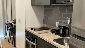 A modern kitchen with a microwave, stove, and sink. There is a dining area with chairs and a table. - Estúdio aconchegante na Sé (São Paulo)