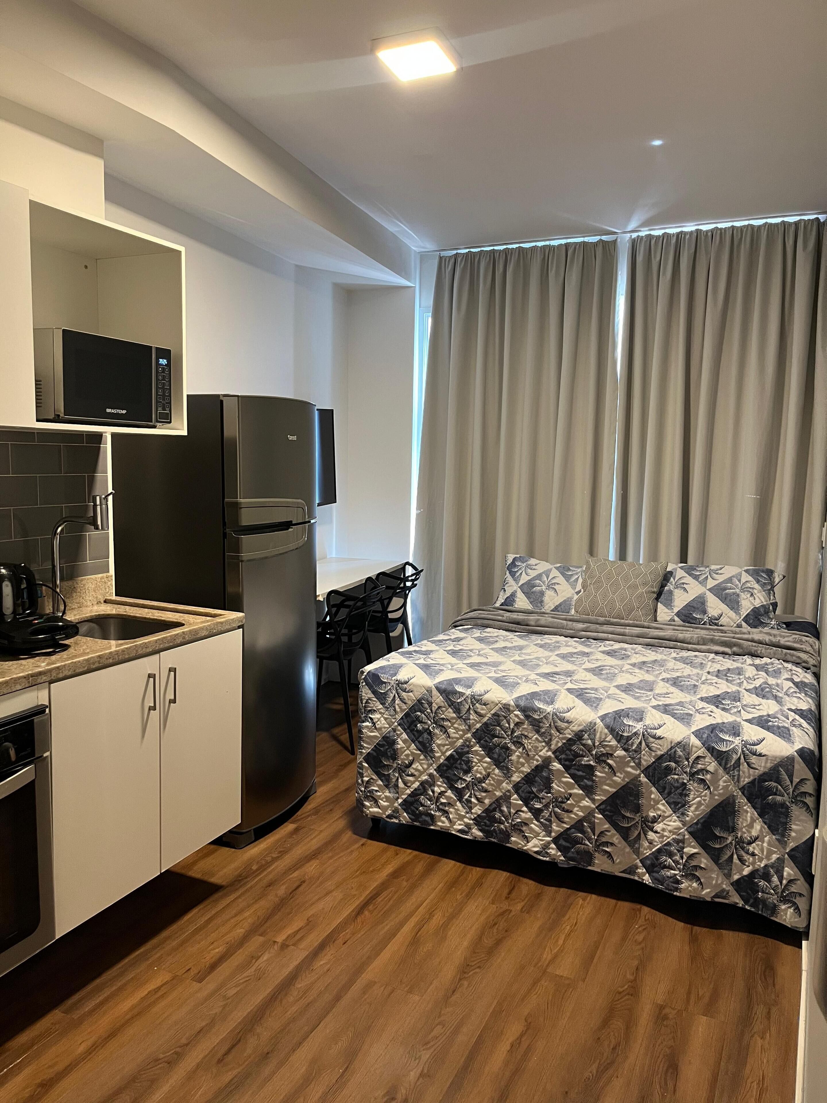Une chambre d’hôtel compacte, dotée d’une kitchenette, d’un lit avec une literie à motifs et offrant une vue sur l’extérieur.