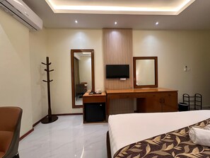 A hotel room with a bed, a desk with a chair, a coat rack, a television, and a mirror. - Grand Luxury Hotel (Semporna)