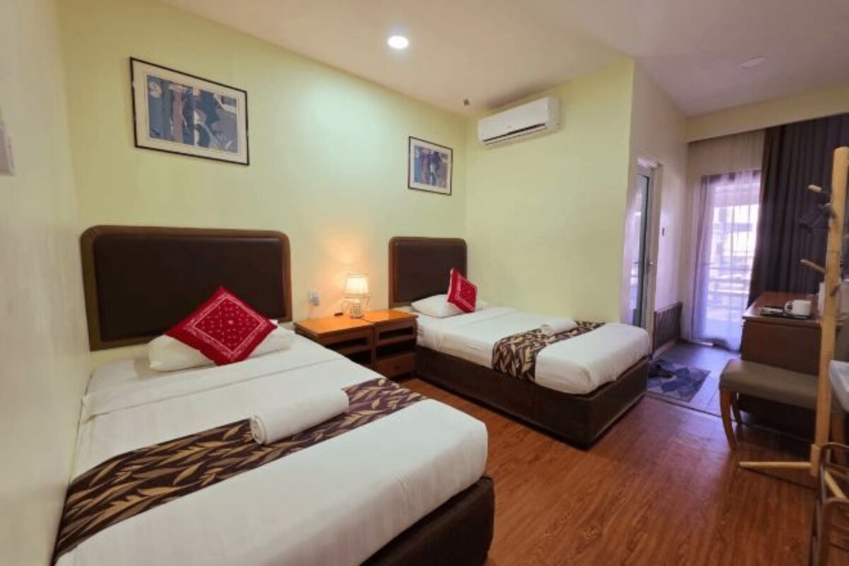 A hotel room with two beds, a desk, a chair, and a window.