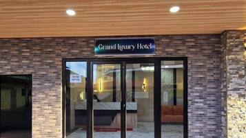 The exterior of the Grand Luxury Hotel with a brick facade, a glass entrance, and a sign indicating the hotel is now open.