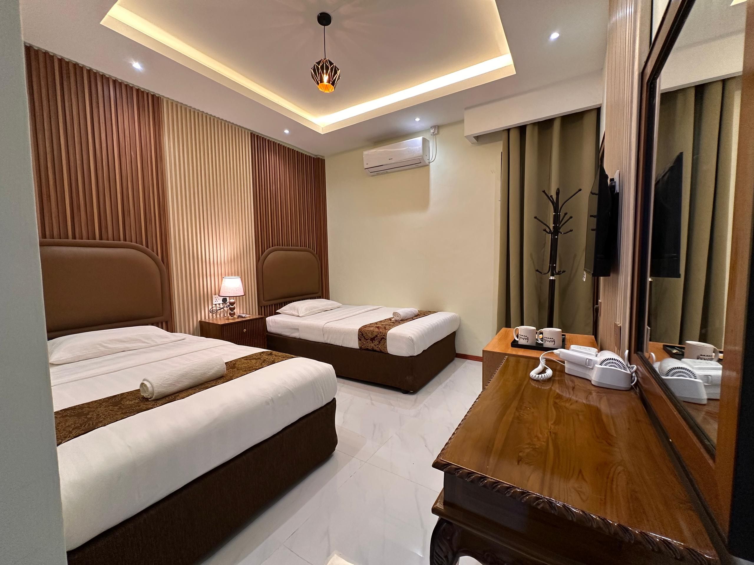 Ein Hotelzimmer mit zwei Betten, einem Nachttisch aus Holz mit Lampe, einem Spiegel und einer Kommode aus Holz mit Telefon und Haartrockner.
