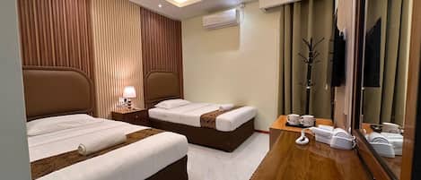 Ein Hotelzimmer mit zwei Betten, einem Nachttisch aus Holz mit Lampe, einem Spiegel und einer Kommode aus Holz mit Telefon und Haartrockner.