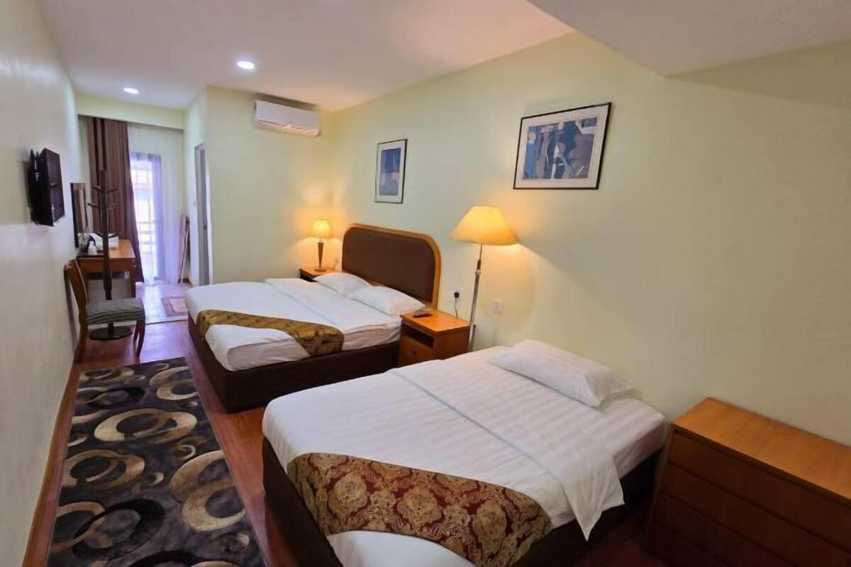 Une chambre d’hôtel avec deux lits, un bureau, une chaise et un tapis à motifs.