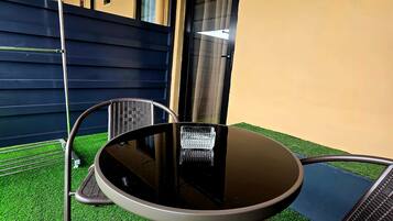 An outdoor seating area with a round table and two chairs, a metal fence, and a building in the background.