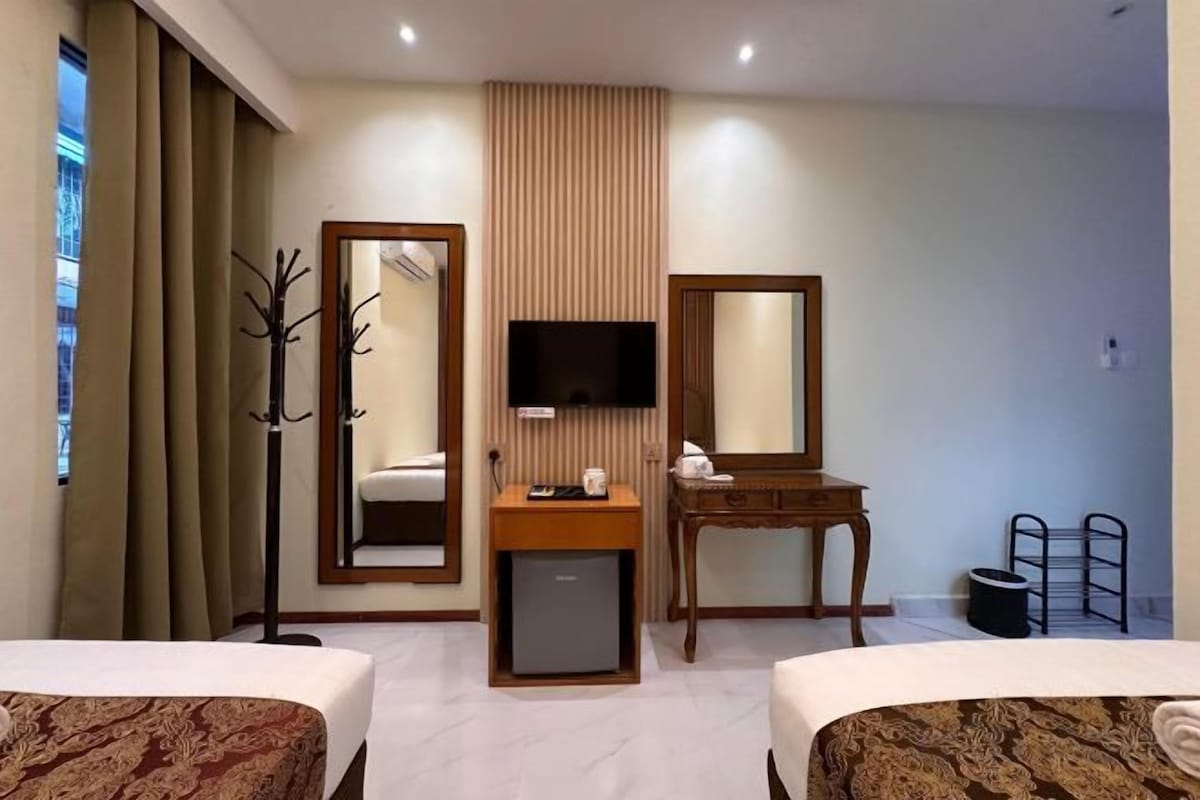 Habitación de hotel con dos camas, un televisor, un escritorio con espejo y un perchero.