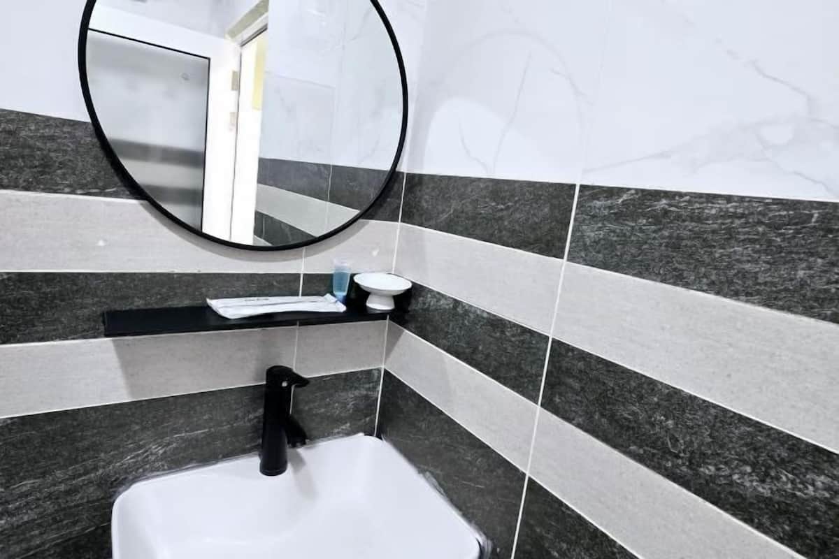 A bathroom with a white sink, black faucet, and a round mirror on the wall.