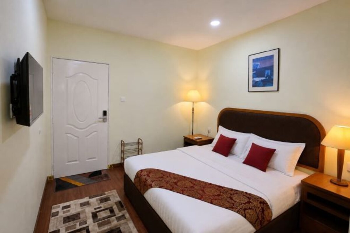 A hotel room with a bed, bedside tables, a lamp, a TV, a door, and a framed picture on the wall.