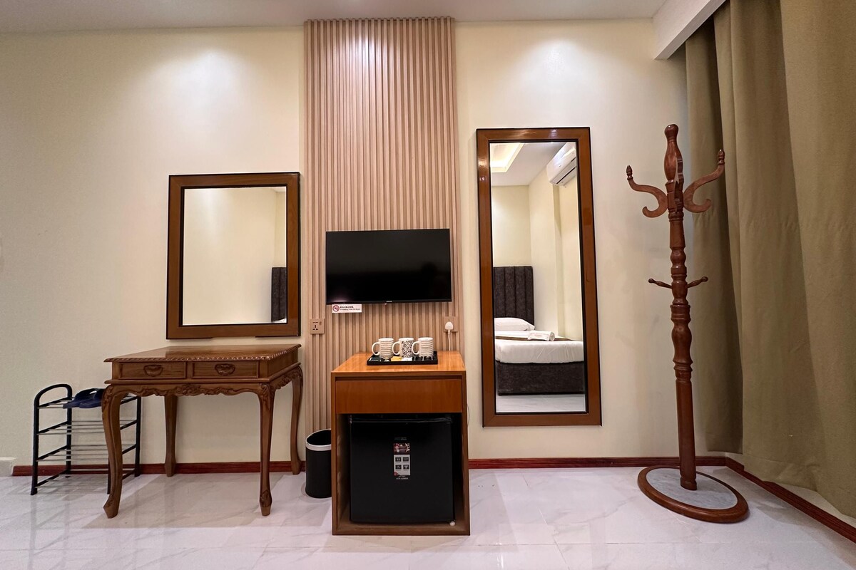 Une chambre d’hôtel équipée d’un lit, d’une télévision, d’un bureau, d’un miroir, d’un porte-manteau et d’un petit réfrigérateur.