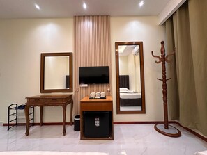 Une chambre d’hôtel équipée d’un lit, d’une télévision, d’un bureau, d’un miroir, d’un porte-manteau et d’un petit réfrigérateur.