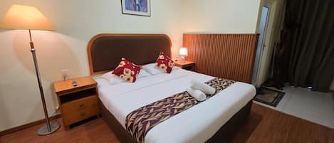 A hotel room with a bed, bedside tables, a lamp, an air conditioning unit, and a window with curtains.
