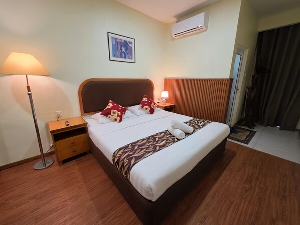 A hotel room with a bed, bedside tables, a lamp, an air conditioning unit, and a window with curtains.