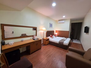 Habitación de hotel con cama, escritorio, silla, mesita de noche, lámpara, espejo y aire acondicionado.