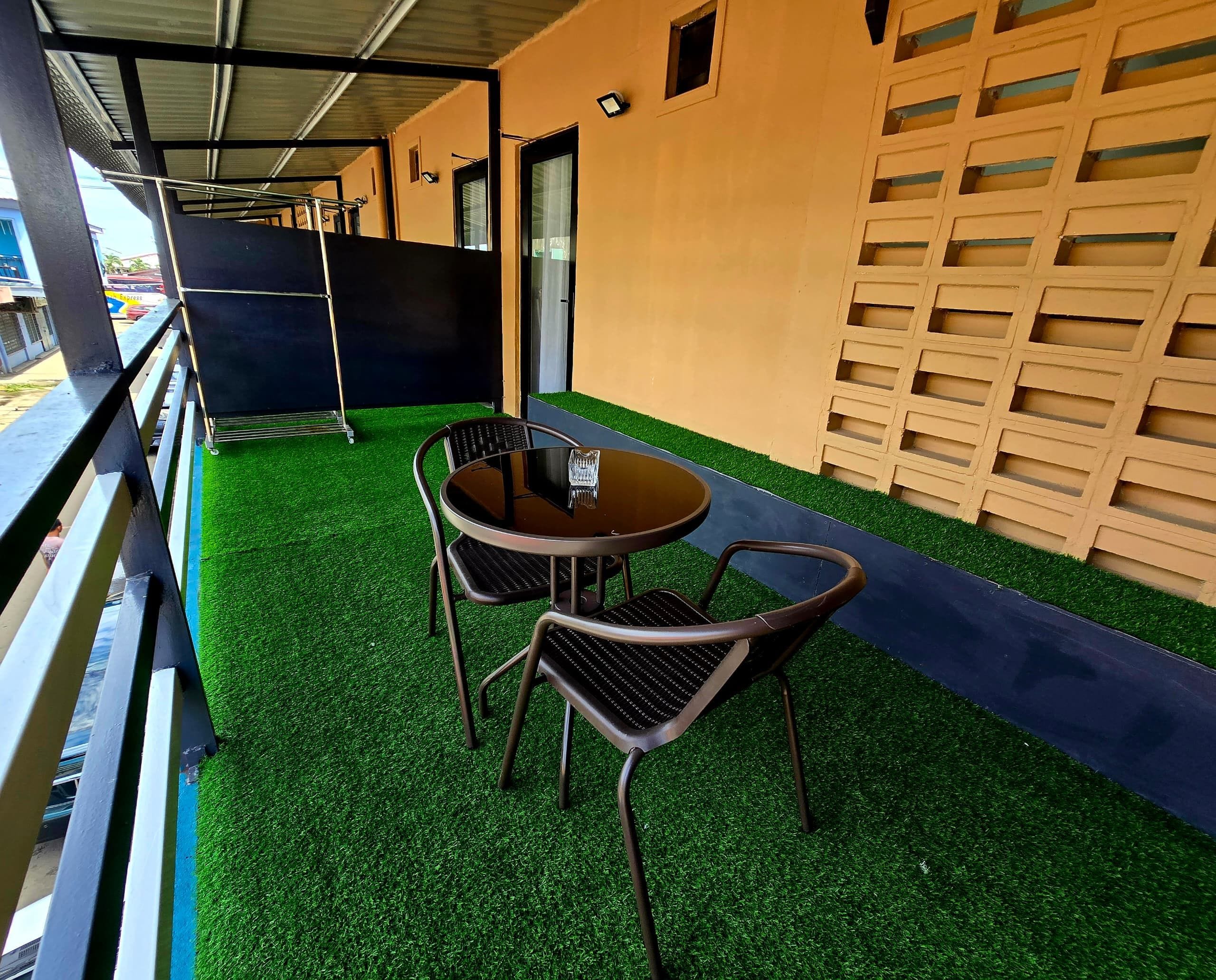 An outdoor seating area with a round table and two chairs, a metal railing, and a wall with a grid pattern.