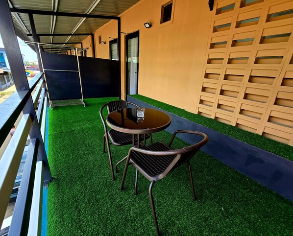 Un espace extérieur aménagé avec une table ronde et deux chaises, une rambarde en métal et un mur orné d’un motif en réseau.