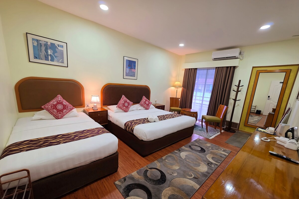 Une chambre d’hôtel avec deux lits, un bureau, une chaise, une lampe, un miroir et un appareil de climatisation.
