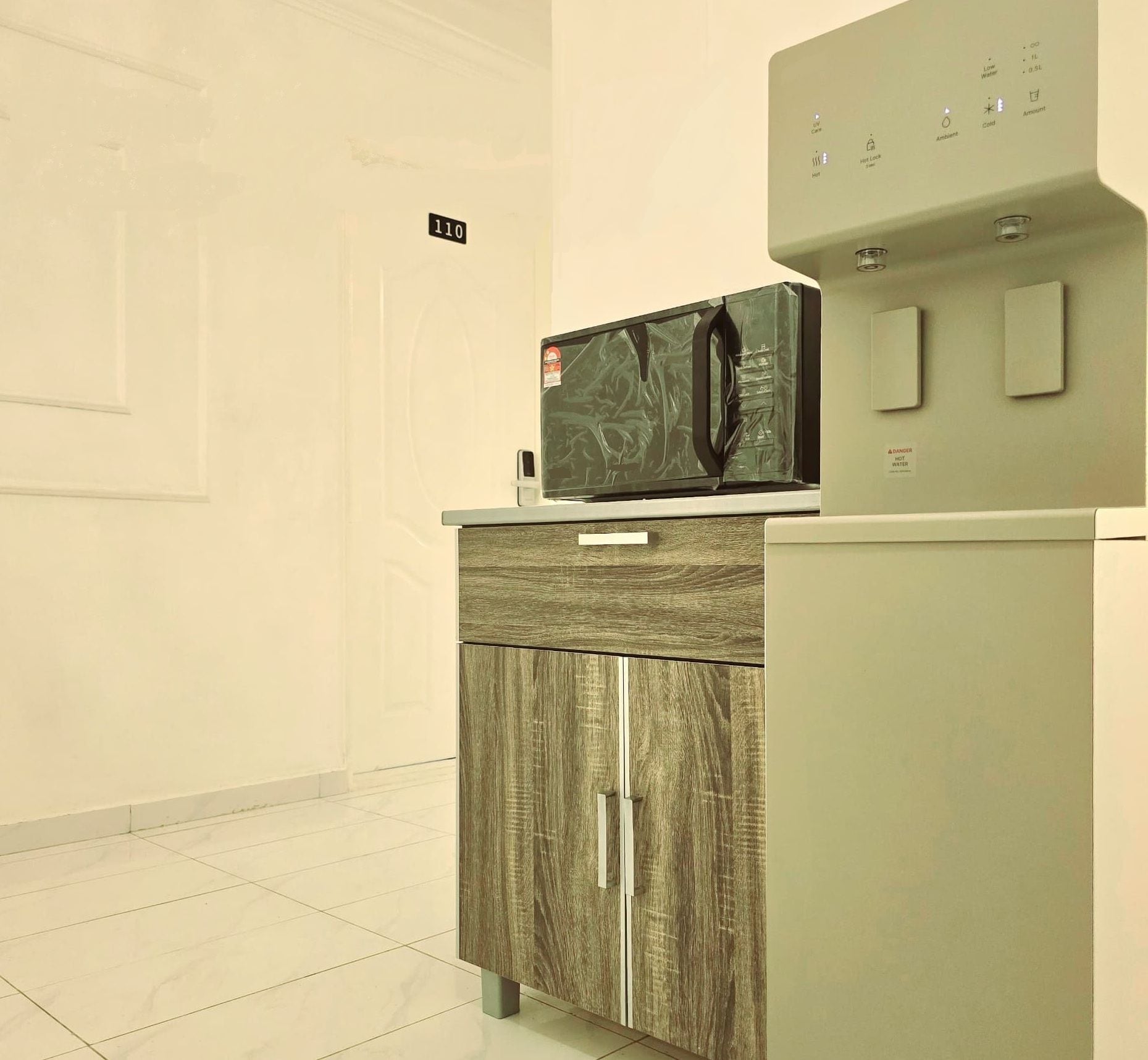 A kitchenette with a microwave on a cabinet, a water dispenser, and a sign indicating room number 110.