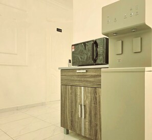 Een kitchenette met een magnetron op een kastje, een waterdispenser en een bordje met het kamernummer 110.