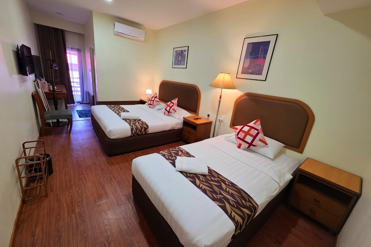 Une chambre d’hôtel avec deux lits, un plancher en bois, un bureau, une chaise, une lampe et un téléviseur.