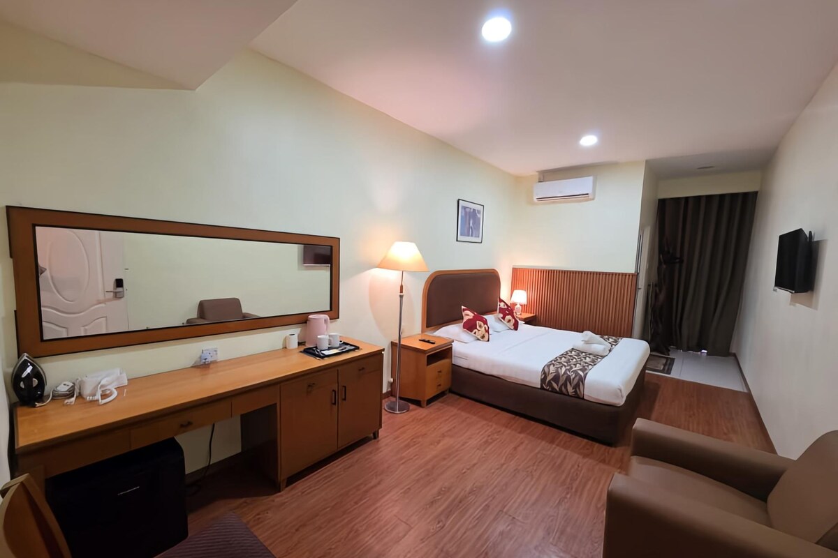 Une chambre d’hôtel équipée d’un lit, d’un bureau, d’une chaise, d’une table de chevet, d’une lampe, d’un miroir et d’un appareil de climatisation.