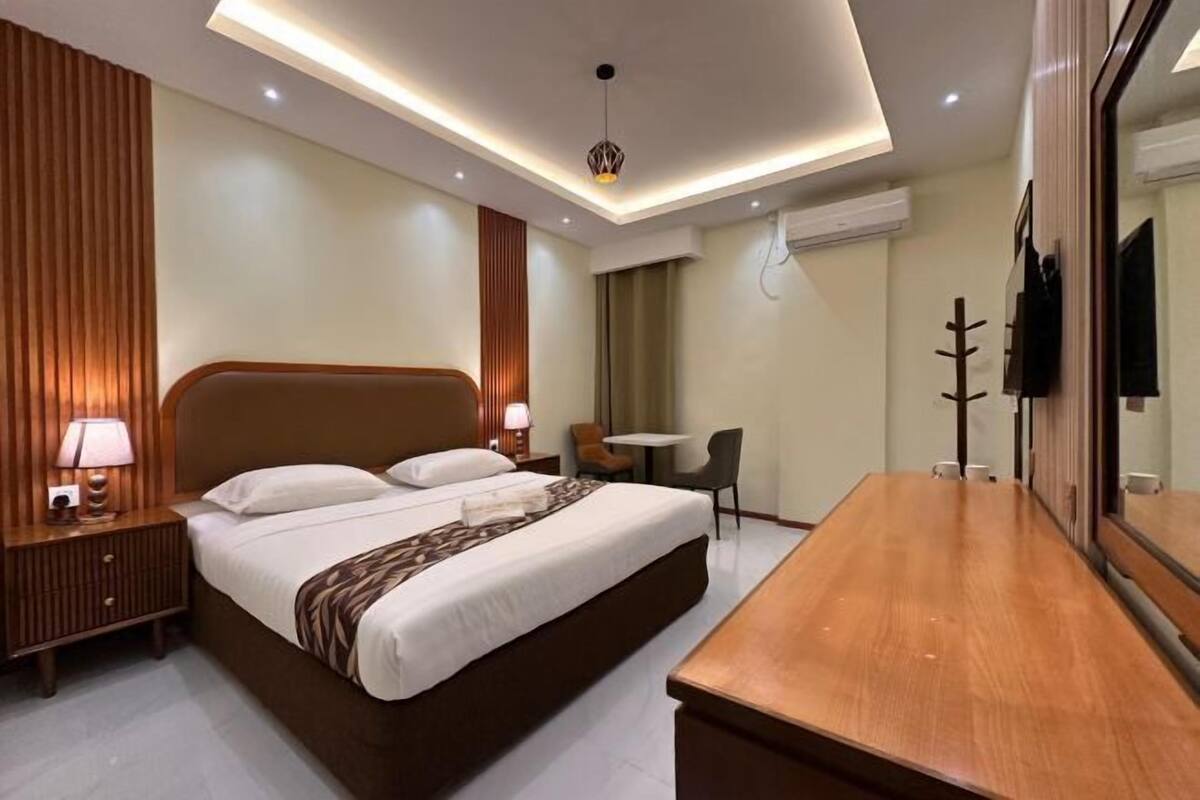 Une chambre d’hôtel avec un grand lit, des tables de chevet, un bureau, une chaise et un téléviseur.