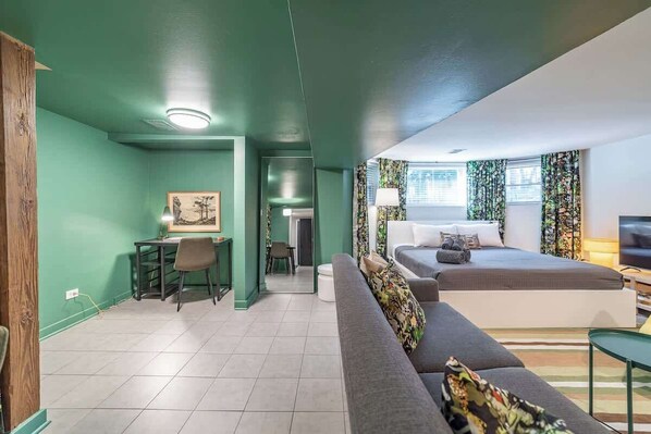 Un espai habitable compacte amb una paret vegetal, un sofà gris, un llit i una petita zona de treball.