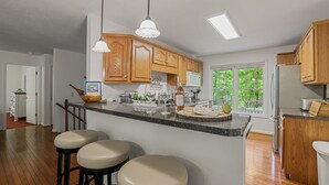 Cucina con mobili in legno, isola centrale con sgabelli, frigorifero e finestra vista sul verde.