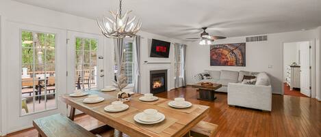 A spacious living room with a wooden dining table set for four, a fireplace, a sofa, and a ceiling fan.
