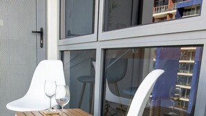 Un'area salotto esterna moderna con una sedia e un tavolo bianchi, due bicchieri da vino e una porta vetrata che dà su un balcone.