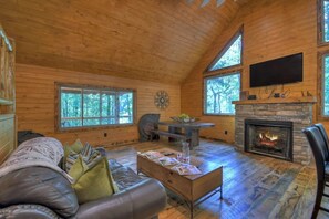 A log cabin interior with a fireplace, a sofa, a dining table, and large windows. - Contemporary Cabin w/ Hot Tub - 2BR, 2BA, Sleeps 8 (Blue Ridge)