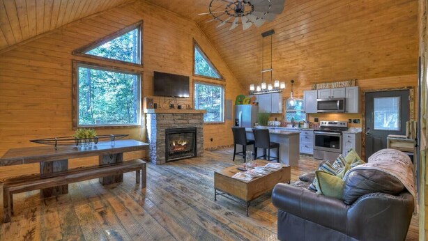 A log cabin interior with a fireplace, wooden floors, a dining area, a kitchen, and large windows. - Contemporary Cabin w/ Hot Tub - 2BR, 2BA, Sleeps 8 (Blue Ridge)
