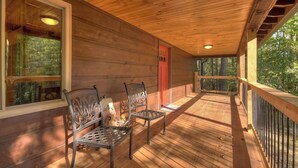 A wooden deck with two metal chairs, a red door, and a view of the forest. - Contemporary Cabin w/ Hot Tub - 2BR, 2BA, Sleeps 8 (Blue Ridge)