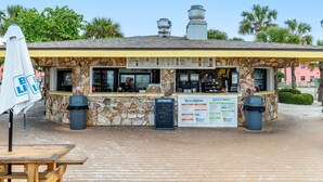 Un ristorante sulla spiaggia con facciata in pietra, tavoli all'aperto e una lavagna con il menu.