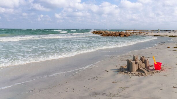 Una spiaggia con un castello di sabbia e un secchiello rosso.