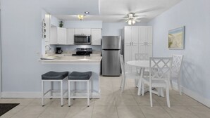 Una cucina moderna con mobili bianchi, un frigorifero in acciaio inossidabile e un'area pranzo con sedie e tavolo bianchi.