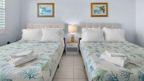 Camera d'albergo con due letti, ognuno con una testiera bianca e cuscini coordinati. Due quadri appesi alla parete, un comodino con una lampada e un pavimento piastrellato.