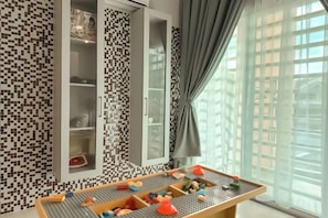 A room with a checkered floor, a table with toys, and a window with curtains.