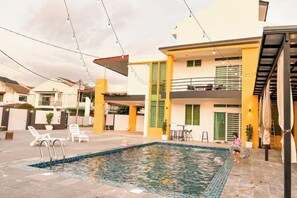 A residential property with a swimming pool, outdoor seating, and a two-story building.
