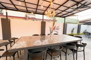 An outdoor dining area with a rectangular table, multiple chairs, and a hanging light fixture.