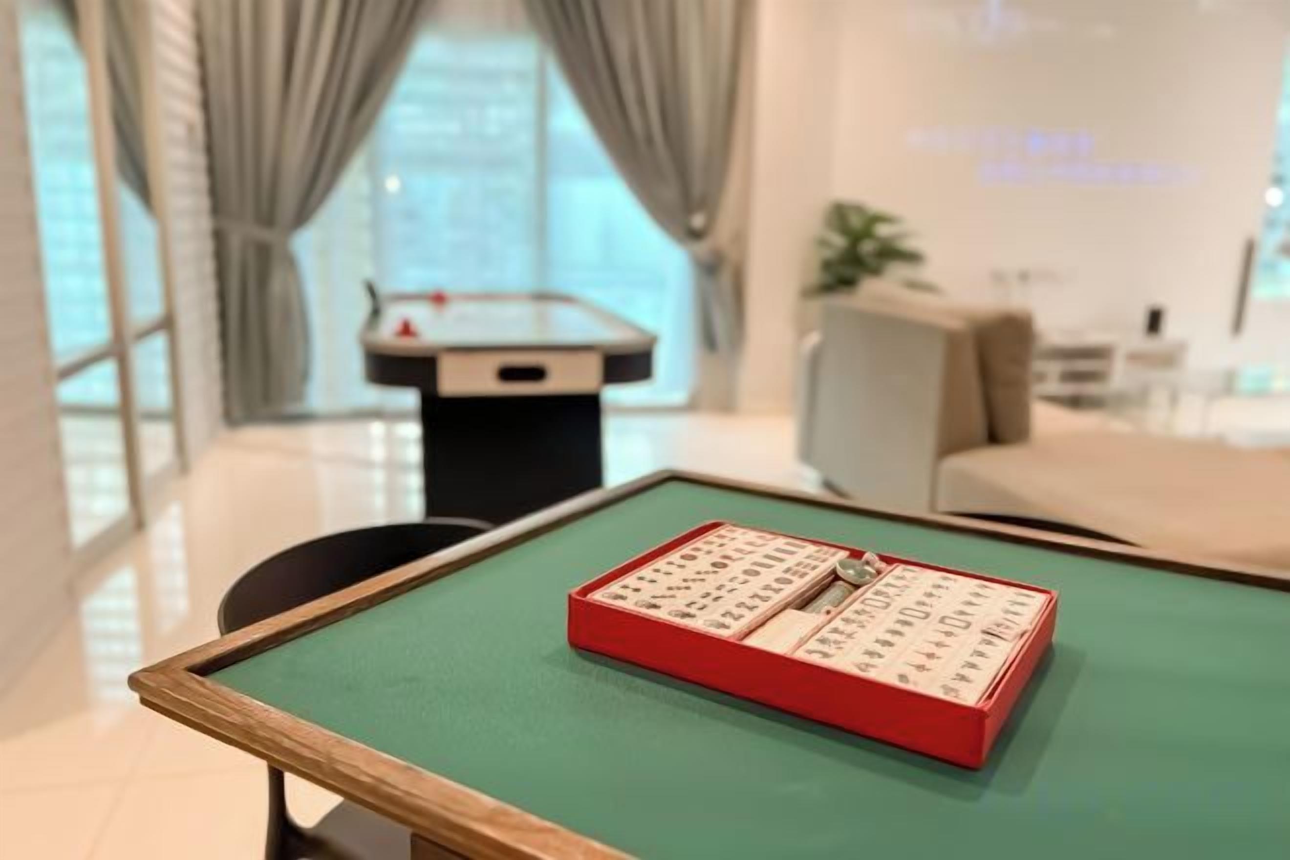 Een kamer met een groene tafel, een rode doos met Chinese karakters, een tafelvoetbaltafel en een bank.