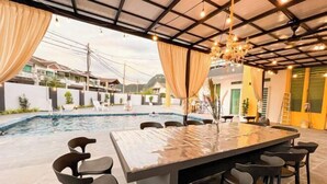 Un área de comedor junto a la piscina con una mesa grande y sillas, una piscina y vistas a edificios residenciales.