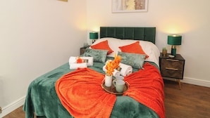 Una camera da letto ordinata con una testiera imbottita verde, una coperta a letto bianco e arancione e due comodini con lampade.