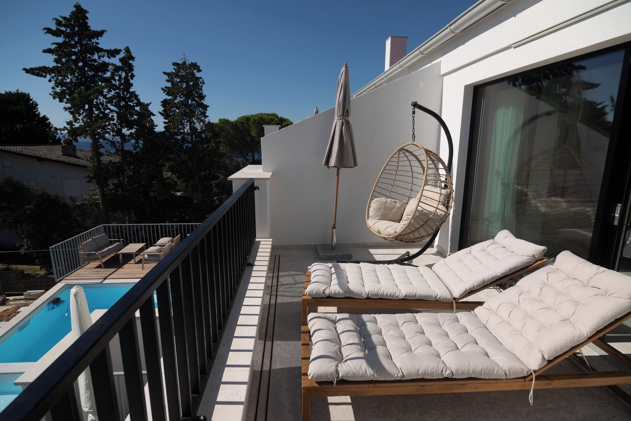 Un balcon avec une piscine, deux fauteuils confortables, un fauteuil suspendu et une grande porte-fenêtre coulissante.
