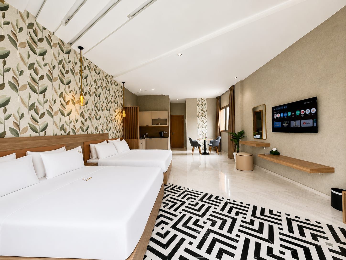 A hotel room with two beds, a TV, a desk, and a kitchen area.