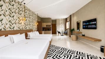 A hotel room with two beds, a TV, a desk, and a kitchen area.